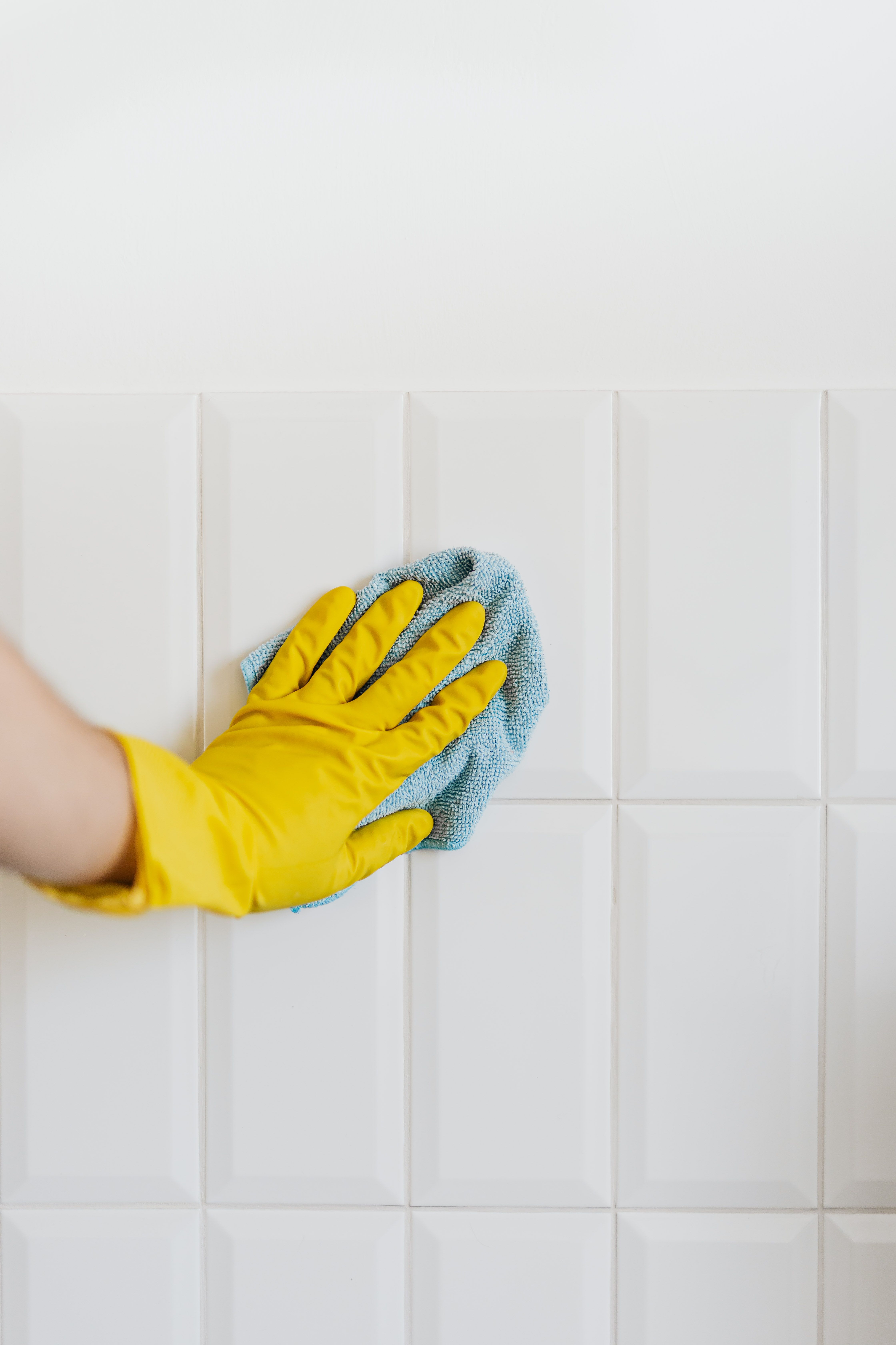 A gloved hand wiping a spotless white tiled wall with a microfiber cloth